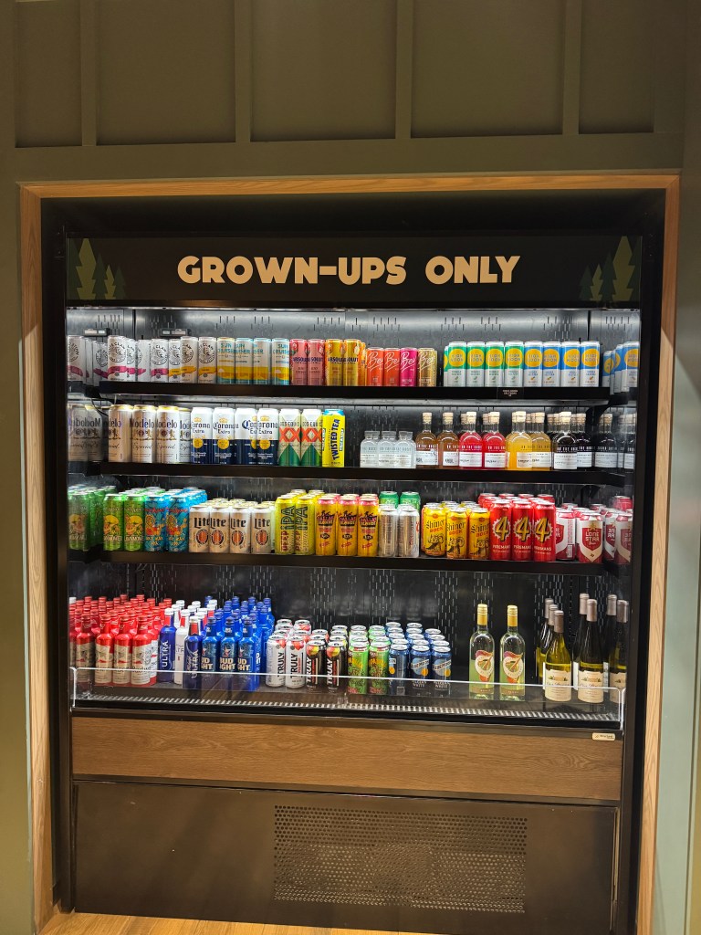 A beverage fridge labeled 'GROWN-UPS ONLY', displaying various alcoholic drinks including beers, seltzers, and cocktails at Great Wolf Lodge in Grapevine, TX
