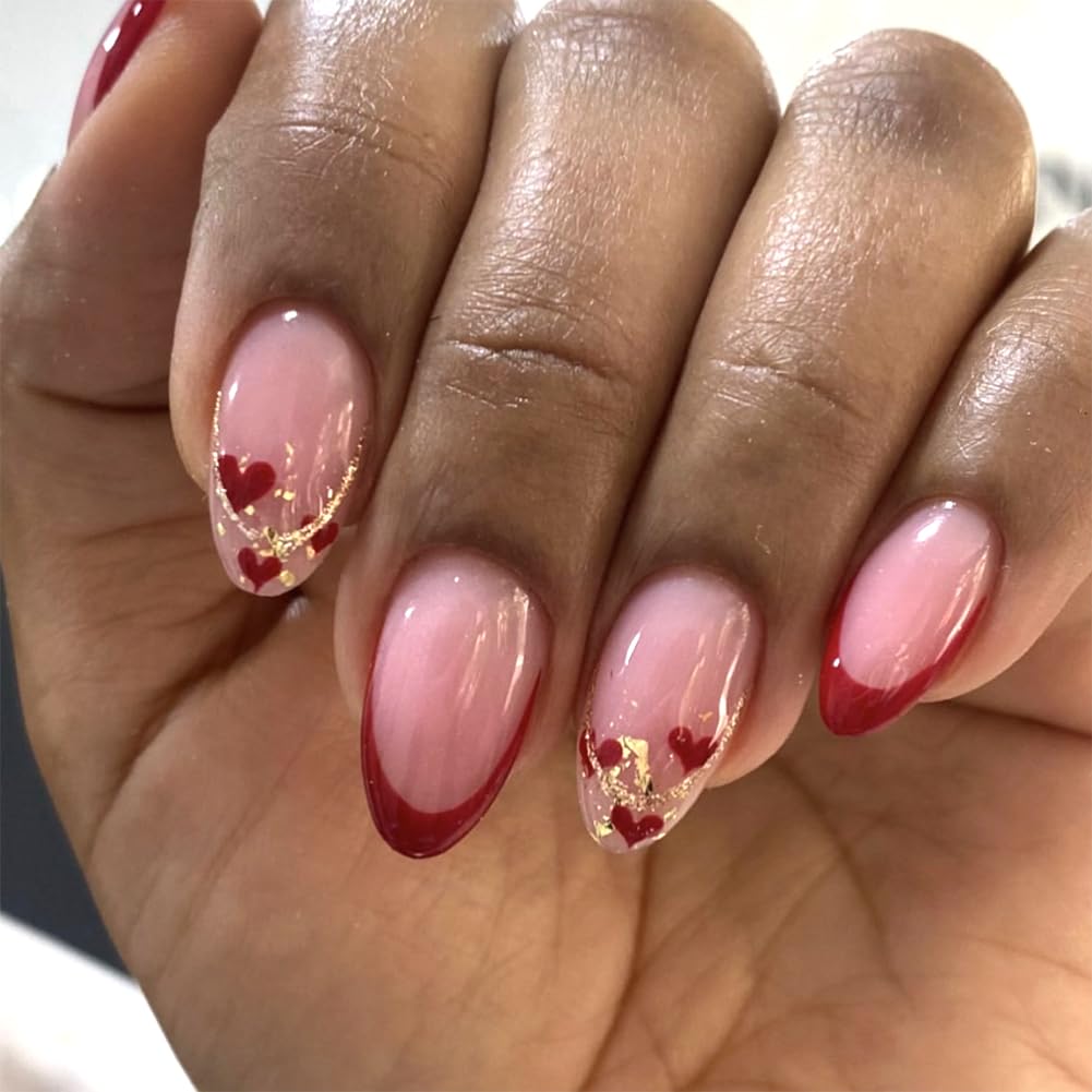 Close-up of manicured nails featuring a pink ombre design with red tips, decorated with small red hearts and gold accents.