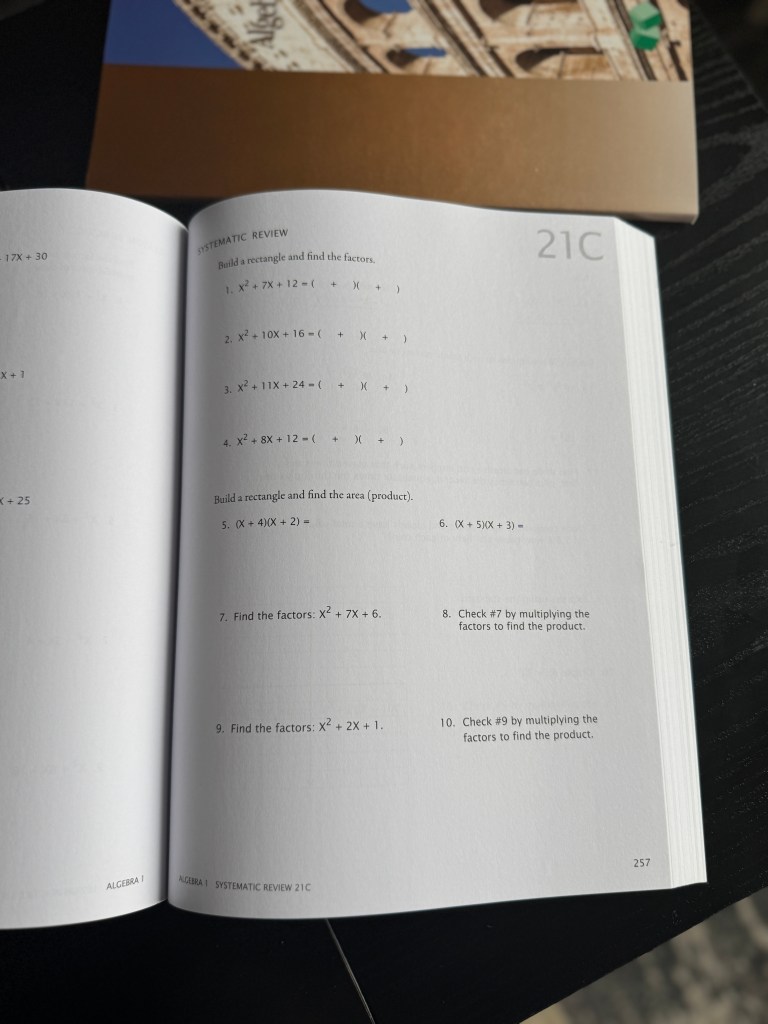 A close-up view of an open Math-U-See Algebra 1 workbook page with problems and systematic review exercises focused on building rectangles and finding factors.