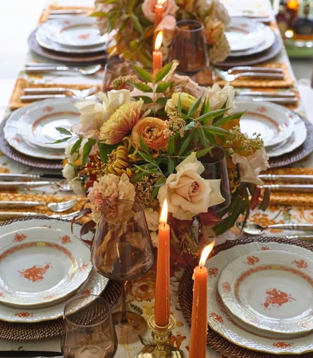 A beautifully styled Thanksgiving table featuring elegant dinnerware, floral arrangements, and warm candlelight. The table is adorned with a floral centerpiece in soft autumn hues, surrounded by plates and glasses, creating an inviting atmosphere.