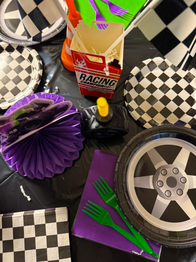 Monster Jam birthday party table setting with racing themed plates, checkered napkins, traffic cone cup, and monster truck centerpiece.