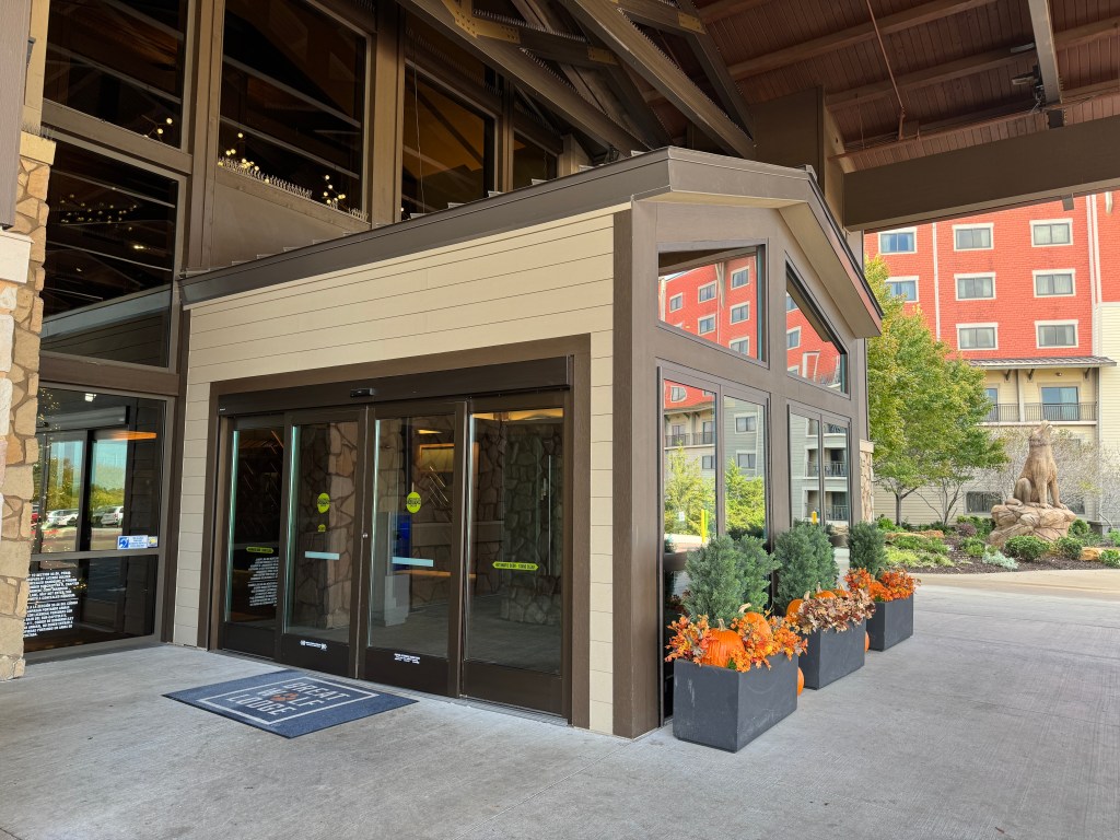 Entrance of Great Wolf Lodge in Grapevine, TX with large glass doors, stone accents, and colorful autumn decorations including pumpkins.