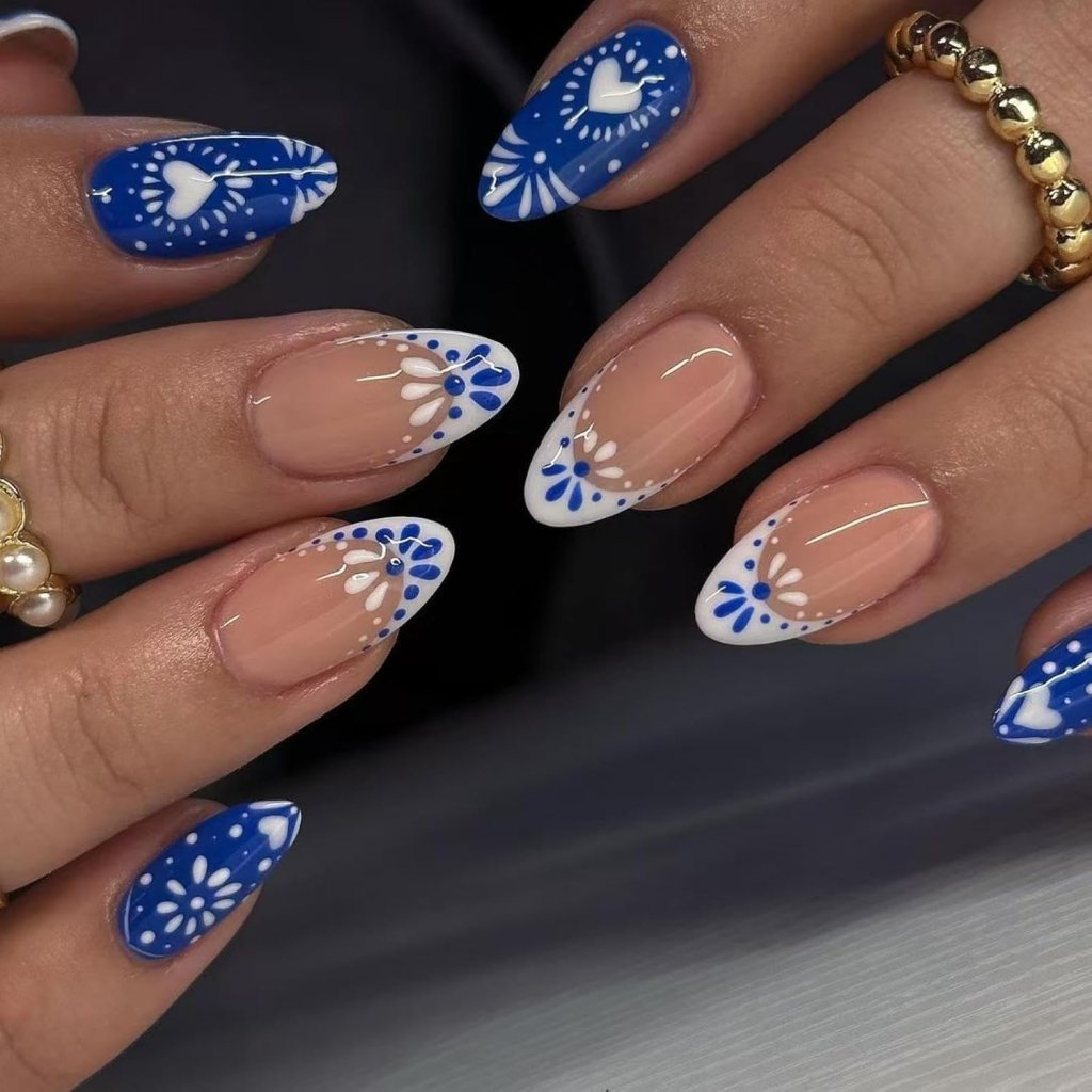 Blue and white folk art almond nails with floral heart-inspired detailing and glossy nude polish.