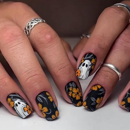 Close-up of hands showcasing matte black nails with floral designs and ghost faces, featuring orange flowers.