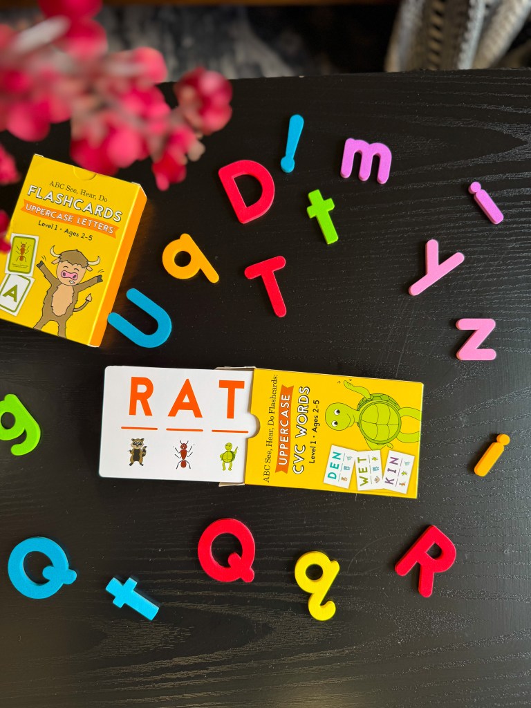 Colorful alphabet letters scattered on a black surface with a children's flashcard showing the word 'RAT' and two additional flashcards, one displaying uppercase letters and the other showcasing CVC words.