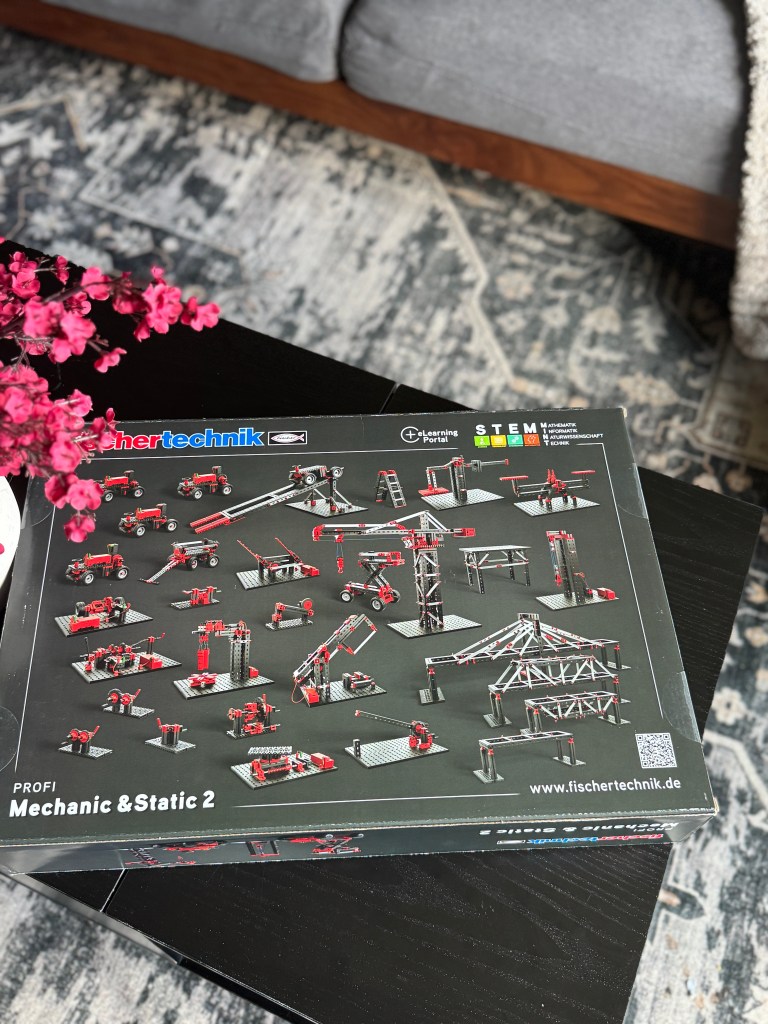 Fischer Technik STEM kit featuring various engineering models displayed on the product box, with a floral arrangement in the foreground.