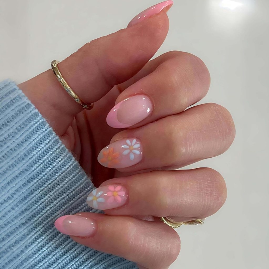 A close-up of a hand with stylish nail art featuring light pink and floral designs on the nails, wearing a delicate gold ring, against a light background.