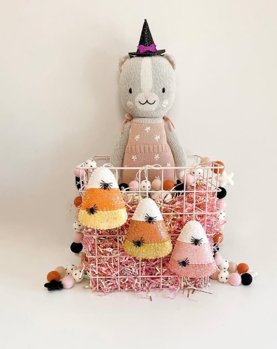 A pastel pink wire basket filled with colorful candy corn decorations and topped with a plush cat doll wearing a black witch hat.