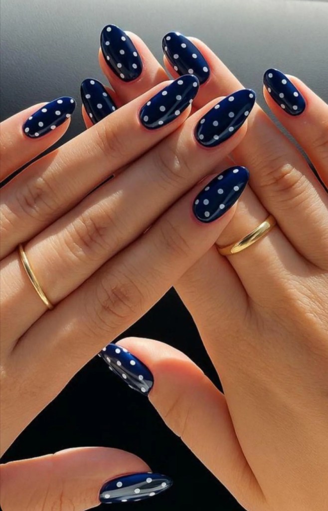 Navy blue polka dot almond nails with glossy cobalt blue polish and small white dot nail art on almond-shaped nails.