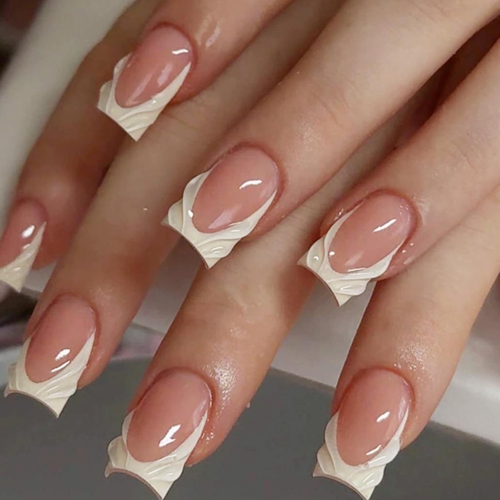 Close-up of manicured hands featuring nude nails with intricate white nail art designs on the tips.
