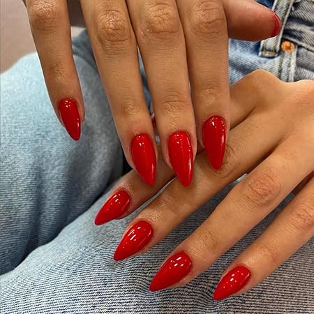 Glossy deep red stiletto nails on hands resting on a denim fabric background.
