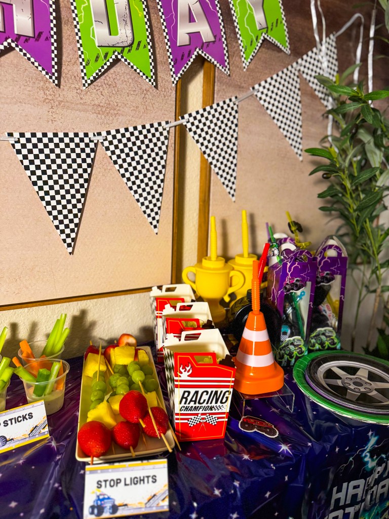 Monster Jam birthday party snack table with racing themed decorations, fruit skewers, veggie cups, and monster truck party favors.