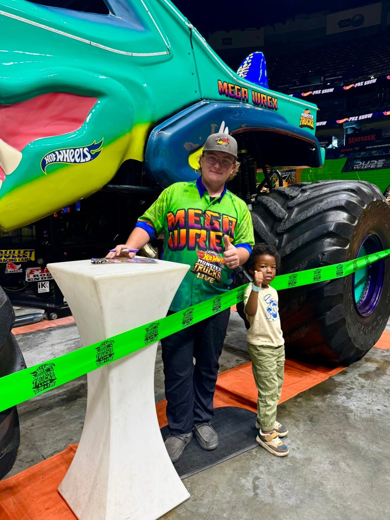 Young child poses with the Mega Wrex driver in front of the colorful monster truck.