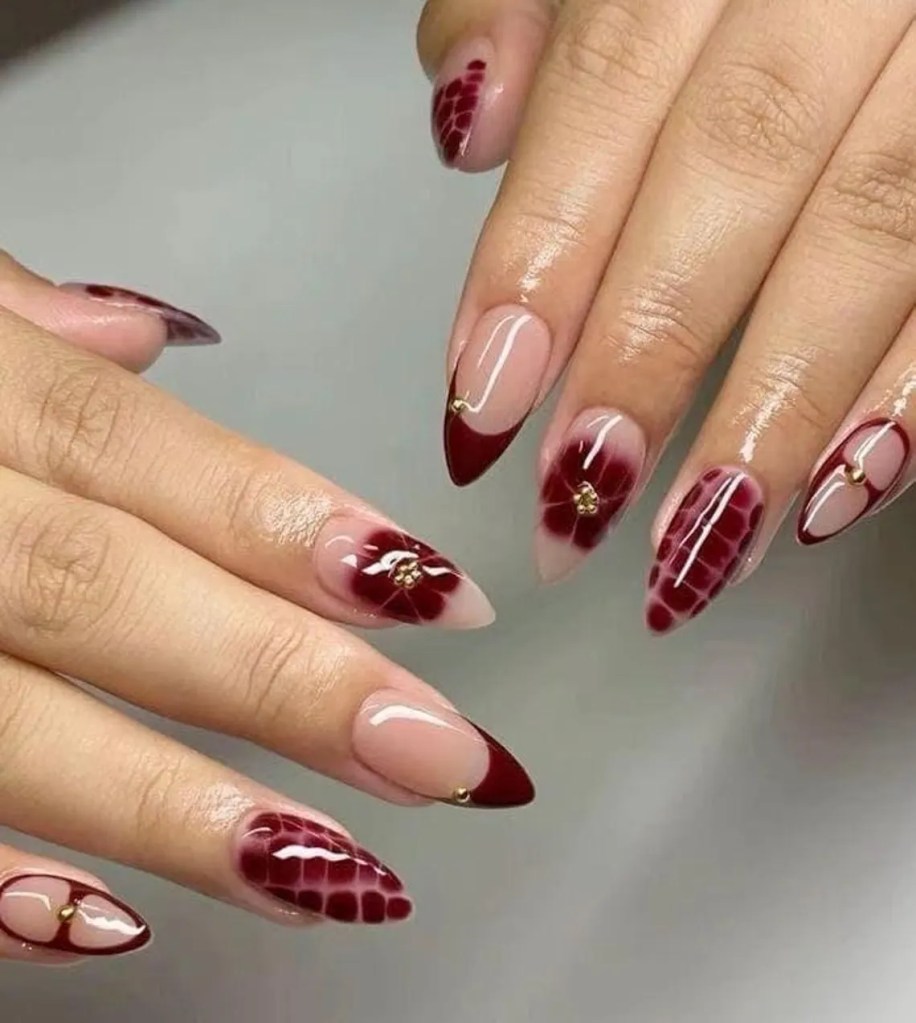Close-up of well-manicured hands showcasing stylish nails with burgundy and nude colors, featuring floral designs and gold embellishments.