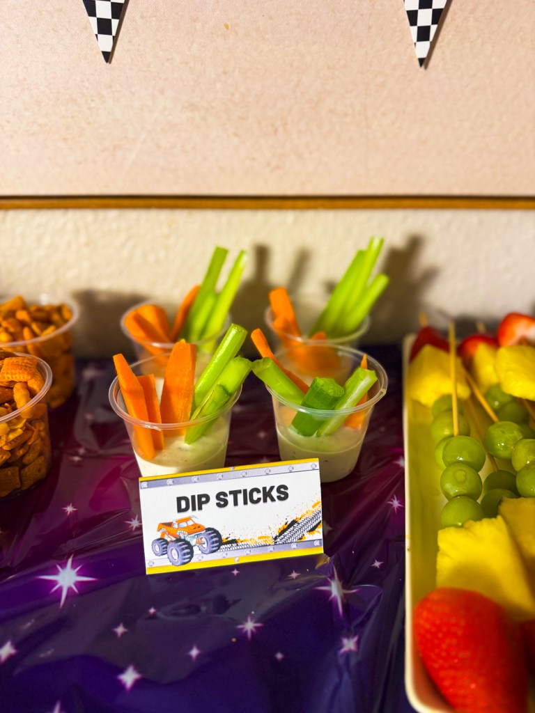 Monster truck birthday party snack idea with dip sticks vegetables and ranch served in cups on a racing themed snack table.