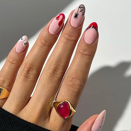 A hand with manicured pink nails featuring a spider web design, red dripping accents, and cute ghost motifs, adorned with a gold ring.