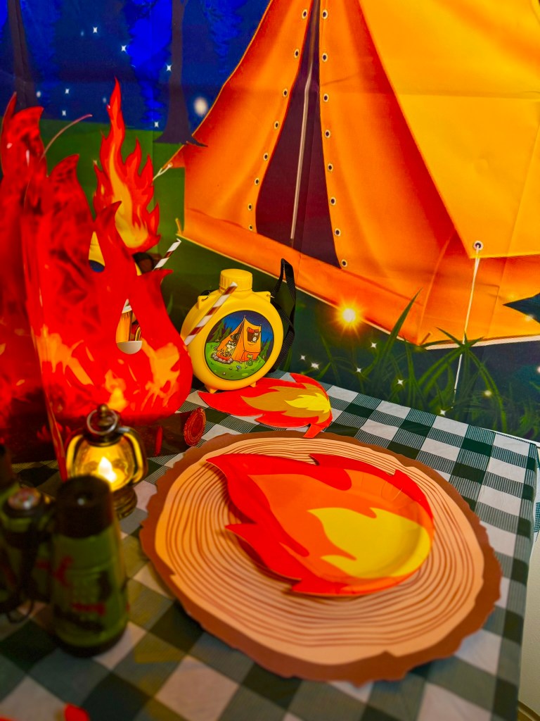 Close-up of fire-shaped plates and log placemats for a camping themed kids birthday party.