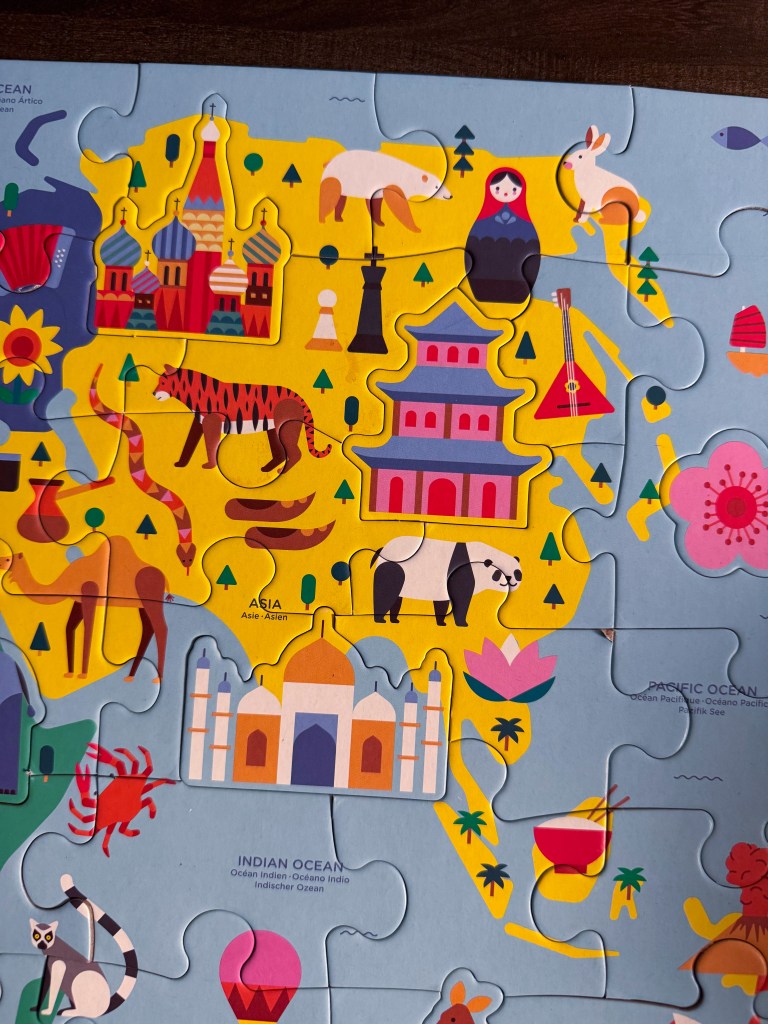 Close-up of Asia on the completed world geography puzzle featuring landmarks, animals and cultural illustrations.