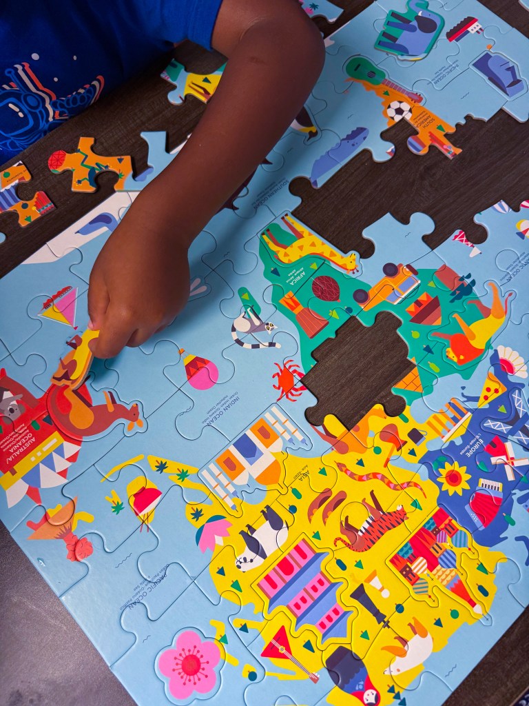 Child working on a colorful world map geography puzzle during a kindergarten homeschool activity.
