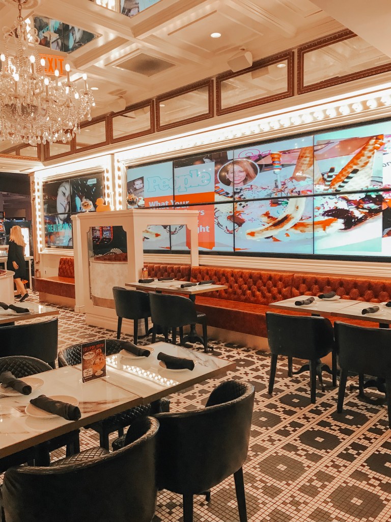 The elegant dining room inside Sugar Factory Biloxi featuring marble tables and red booths.