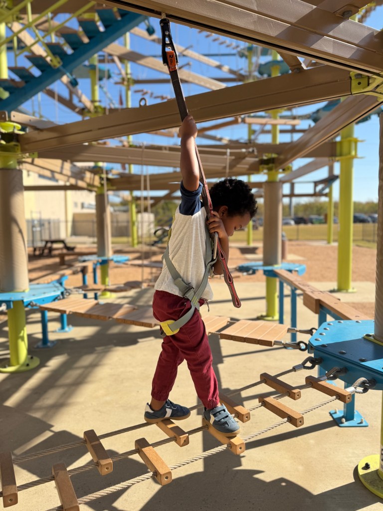 Preschooler carefully crossing a suspended rope bridge on the outdoor ropes course at Great Wolf Lodge Grapevine.