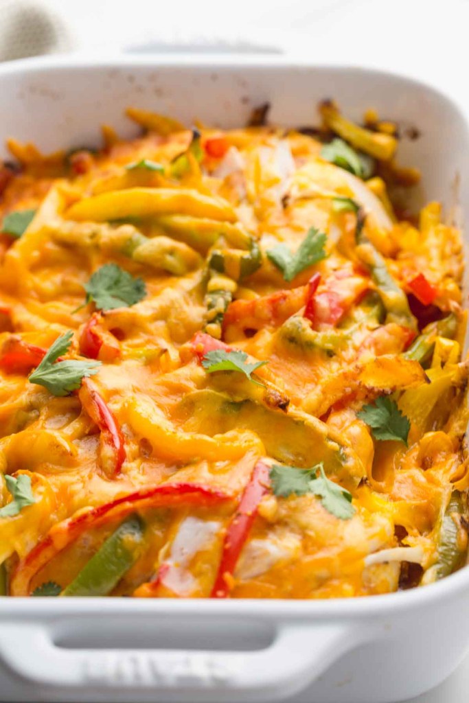 A cheesy chicken casserole with colorful bell peppers and fresh cilantro, baked to perfection in a white dish.