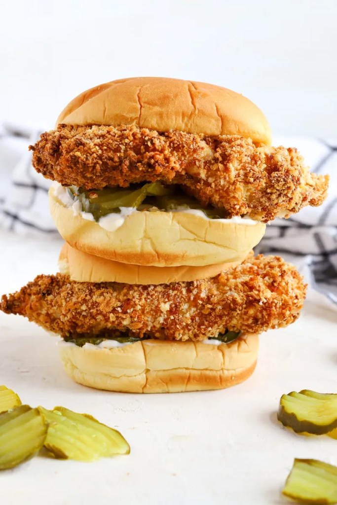 A stacked chicken sandwich featuring crispy fried chicken fillets, pickles, and creamy sauce on toasted buns.