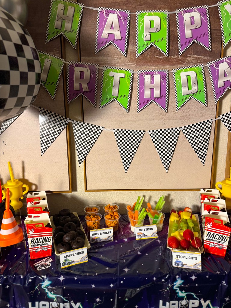 Monster Jam birthday party snack table with racing themed decorations, labeled snacks, and monster truck party banner.