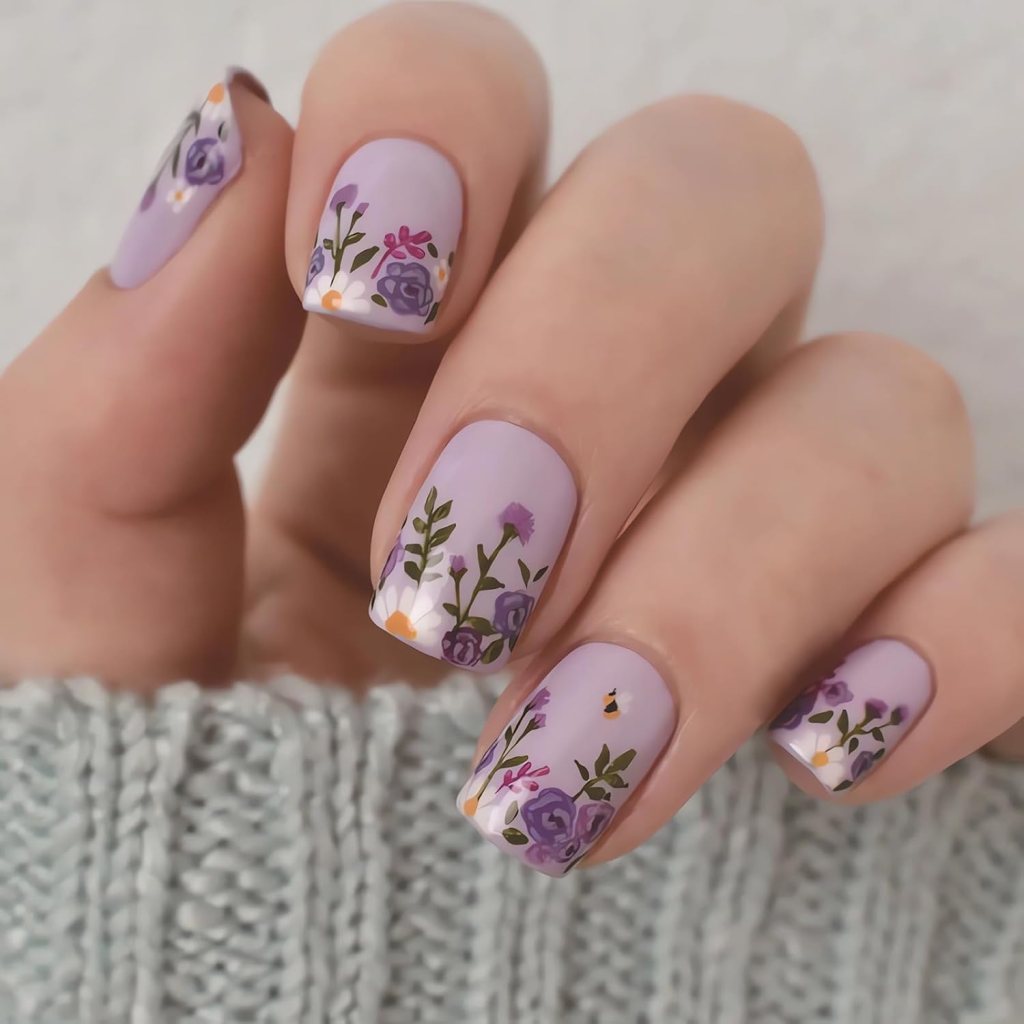 A close-up of a hand holding a purple sweater, showcasing beautifully manicured nails with floral designs in shades of purple, pink, and green.