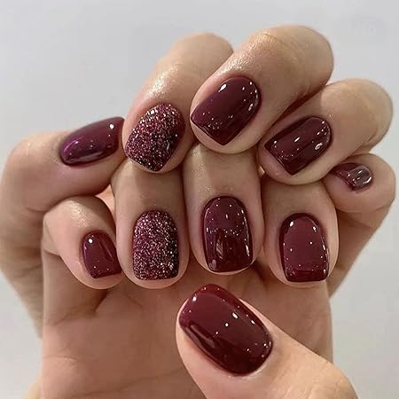 Manicured nails in deep burgundy with a mix of glossy and textured finishes, featuring one accent nail with glitter.