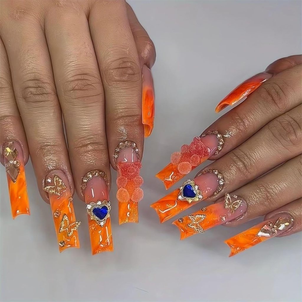 Long orange acrylic nails with rhinestones, gems, and 3D charm accents