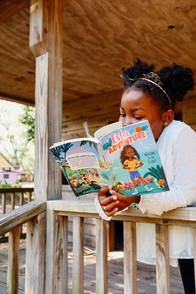 Young girl reading the Isla of Adventure chapter book while sitting on a wooden porch.