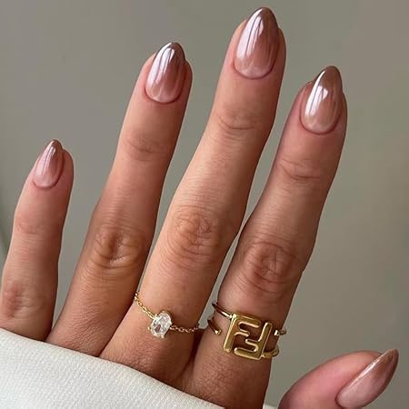Close-up of a woman's hand displaying elegant almond-shaped nails with a glossy nude finish, adorned with delicate rings.
