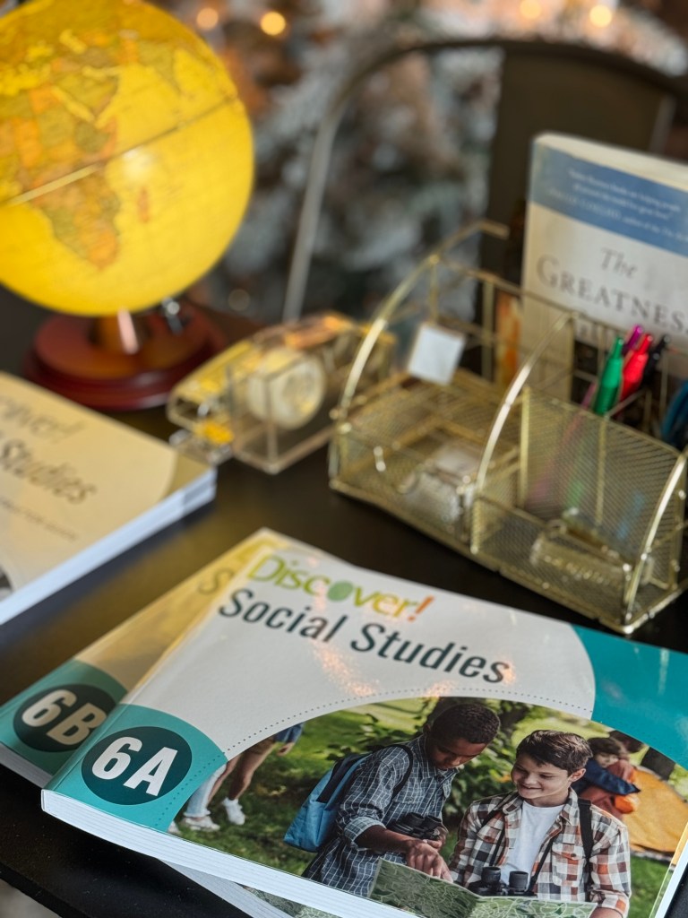 A globe, books, and school supplies on a table, featuring the curriculum 'Discover! Social Studies Grade 6'. Two children are visible in the foreground, engaged with the materials.