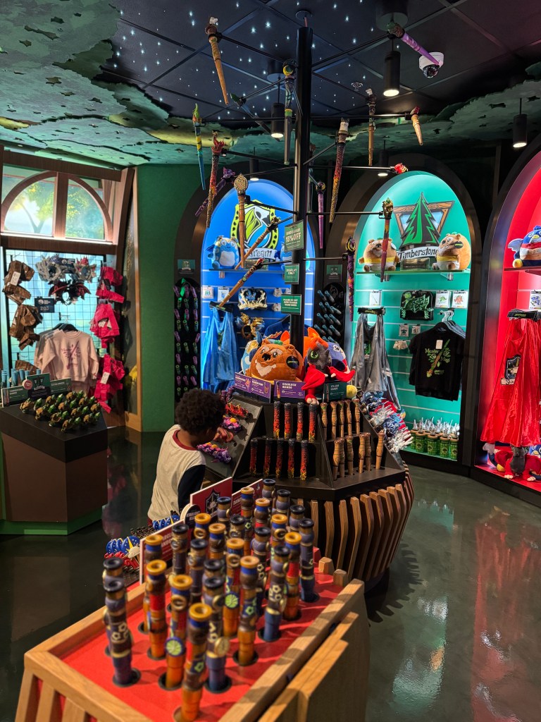 A child browsing a store at Great Wolf Lodge, surrounded by colorful merchandise including wands, plush toys, and themed clothing.