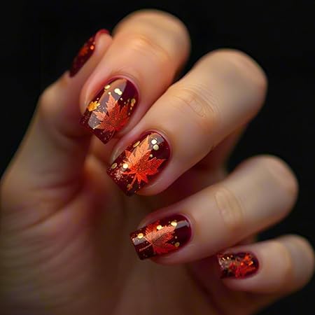 Close-up of manicured nails featuring deep burgundy polish with metallic gold maple leaf designs and sparkling accents.