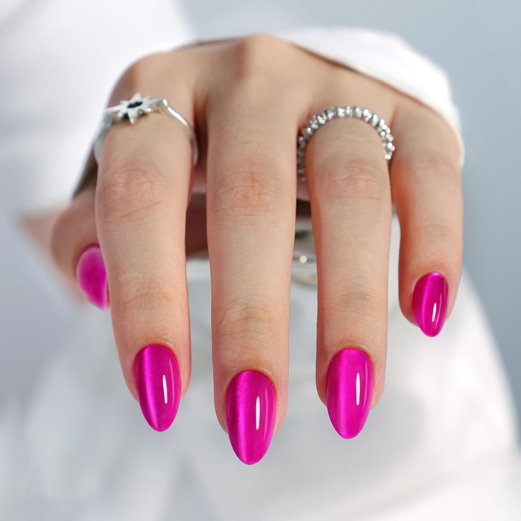 A close-up of a hand with long, almond-shaped nails painted in bright pink polish, showcasing elegant rings on two fingers.