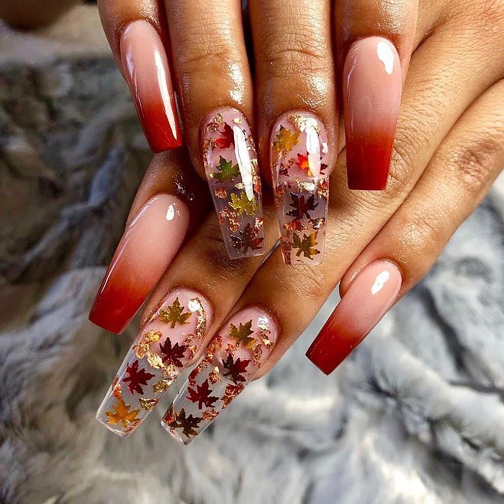 Elegant long nails featuring an ombre effect with red tips and a transparent base adorned with gold and colorful fall leaf designs.