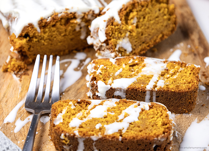 Slices of pumpkin bread drizzled with a white icing glaze on a wooden cutting board.