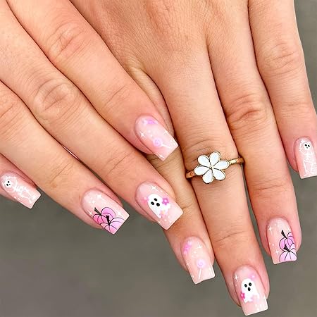 Pastel pink nails featuring cute ghost faces and floral accents, adorned with a delicate ring.