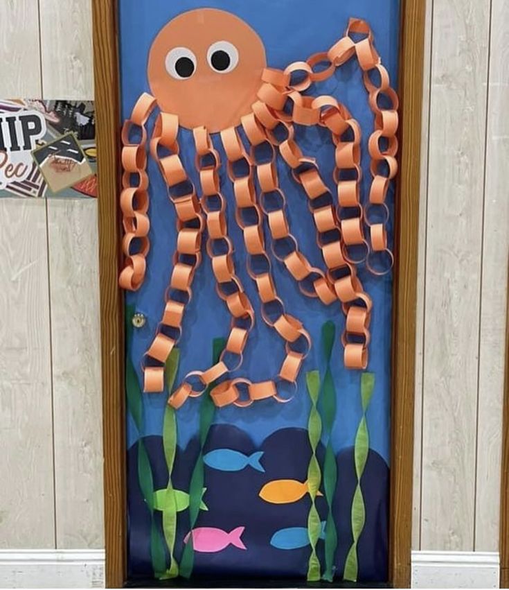 A decorative door covered with blue paper featuring an orange octopus made of paper chains and large googly eyes, surrounded by colorful fish and green seaweed cutouts.