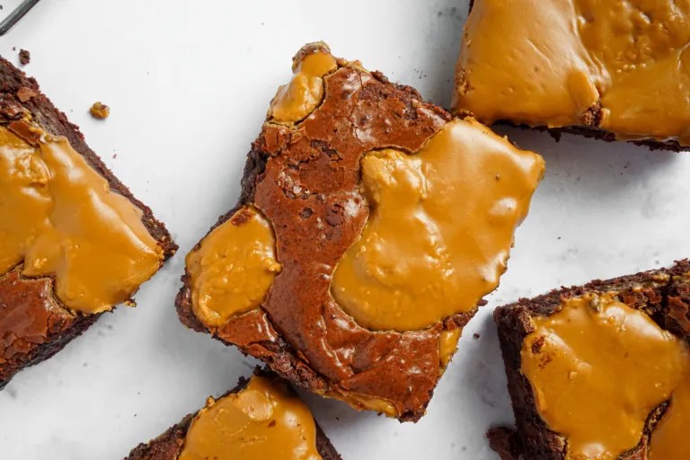 Close-up of fudgy brownies topped with a glossy layer of caramel sauce.