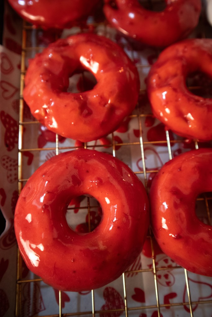 A tray of freshly glazed red donuts placed on a cooling rack.