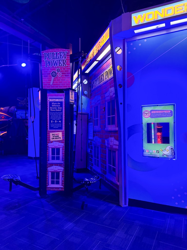 An indoor amusement area featuring a 'Pulley Power' attraction with colorful signage and equipment in a blue-lit environment.