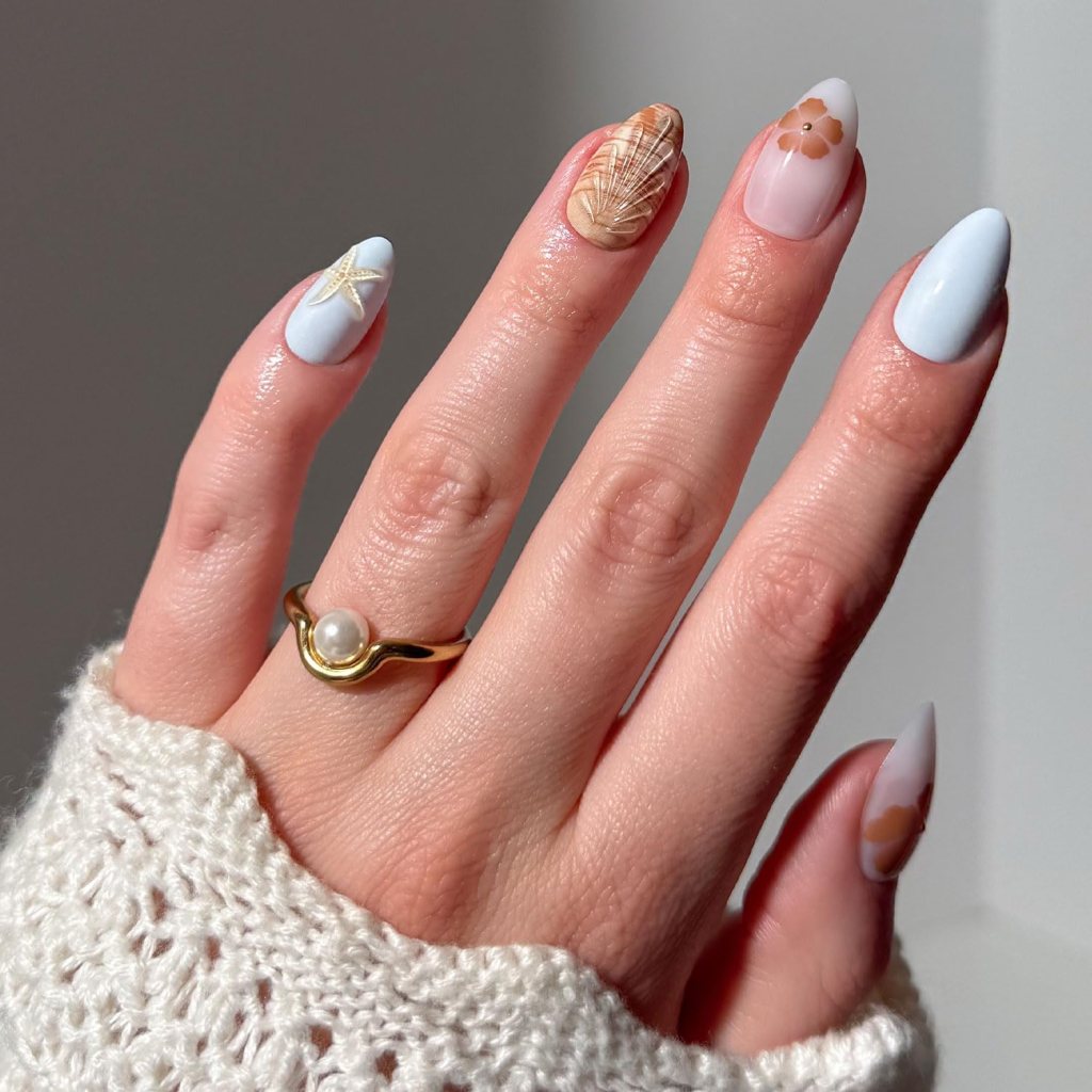 Classy beach-inspired ocean nails with soft blue polish, seashell textures, floral accents, and elegant coastal manicure design
