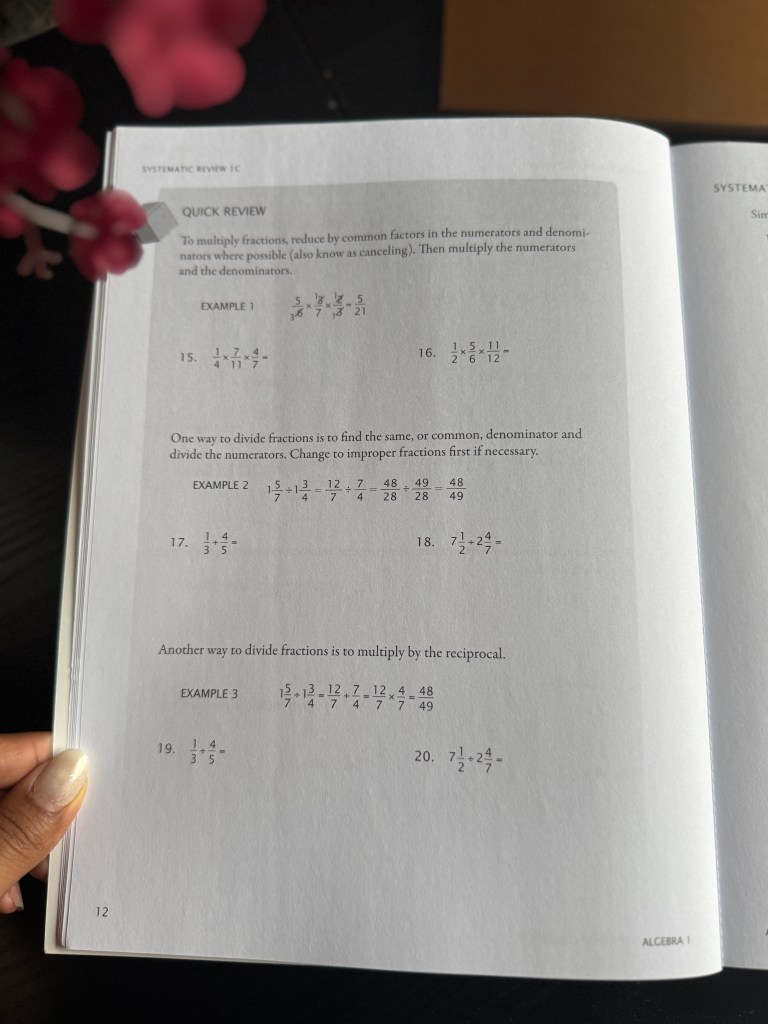 A close-up image of an open math textbook page featuring a section titled 'Systematic Review 1C' with examples and exercises focused on reducing and dividing fractions, accompanied by hand-written answers.