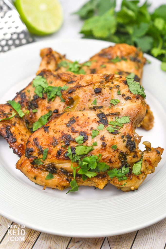 Grilled cilantro lime chicken thighs garnished with fresh cilantro and served on a white plate, with a lime wedge in the background.