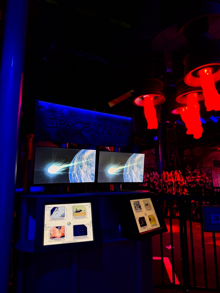 A display booth for a 'Space Trivia' game featuring two screens showing an animated comet and Earth, accompanied by interactive trivia options.