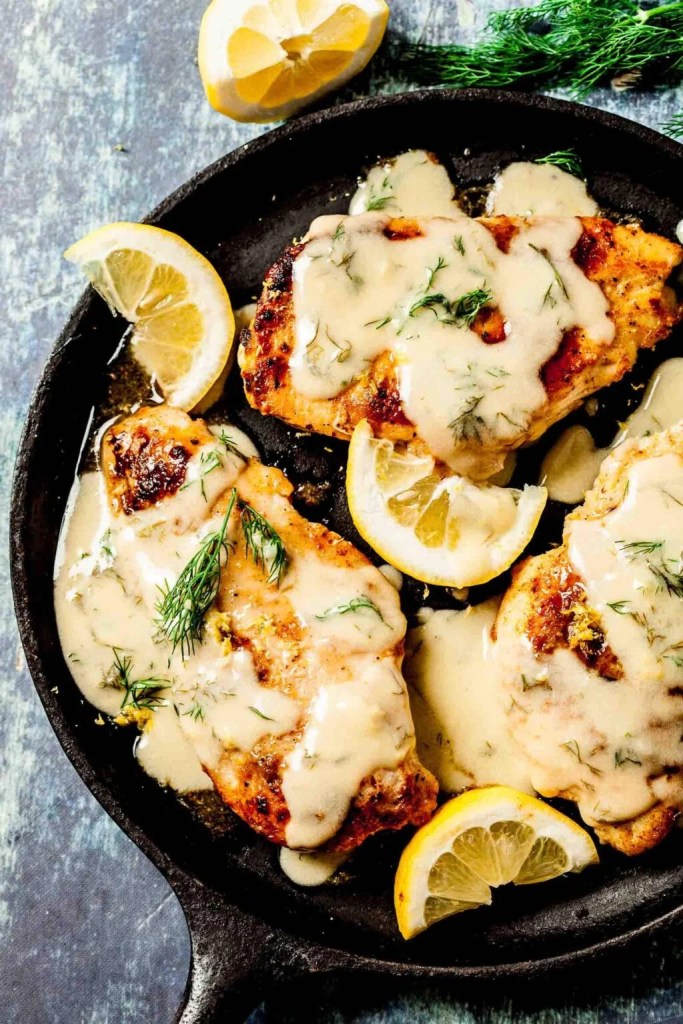 Pan-seared chicken breasts topped with a creamy sauce and garnished with fresh dill and lemon slices.