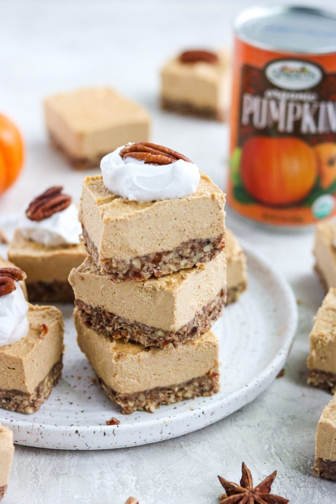 Stack of no bake pumpkin cheesecake bars with a pecan crumble crust, topped with whipped cream and a pecan, next to a can of pumpkin.